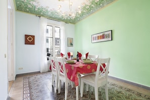 Een eethoek met een tafel voor vier personen, witte stoelen, een rode tafelkleed en een kroonluchter.