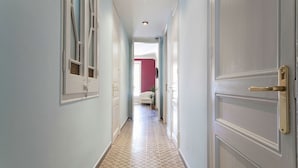 Un pasillo con piso estampado, una puerta blanca con picaporte de latón y vista a una habitación con pared roja y cama.