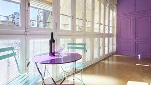 A room with large windows, a purple table with a bottle and glass, and teal chairs.