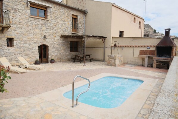 A stone building with a pool, outdoor seating, and a barbecue area.