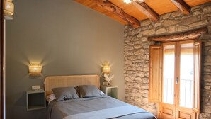 Une chambre à coucher avec un lit, deux lampes de chevet, une table de chevet, un mur en pierre et une porte en bois donnant sur un balcon.