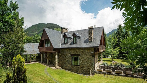 Una casa de piedra con techo inclinado, una terraza de madera y un sendero de piedra que conduce a la entrada.