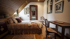 A cozy bedroom with a wooden ceiling, a large bed with a patterned bedspread, a wooden desk, and a chair.