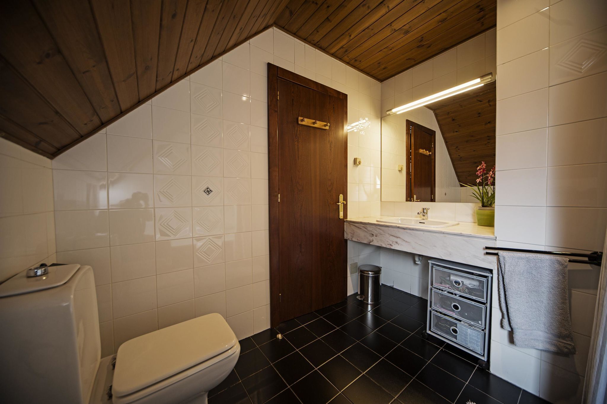 Un baño con inodoro, lavabo, espejo y un cubo de basura.