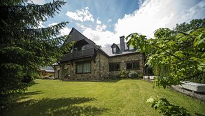 A stone house with a balcony, surrounded by a well-maintained lawn and trees.