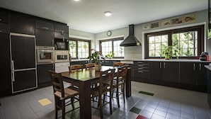 Una cocina moderna con armarios oscuros, una mesa de comedor, sillas, un microondas, un horno y un amplio ventanal con plantas.