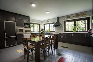Une cuisine moderne avec des meubles de couleur sombre, une table à manger, des chaises, un four à micro-ondes, un four traditionnel et une grande fenêtre agrémentée de plantes.