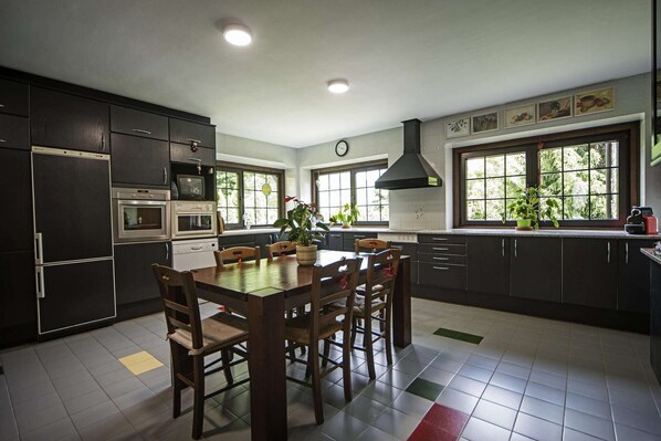 Una cocina moderna con armarios oscuros, una mesa de comedor, sillas, un microondas, un horno y un amplio ventanal con plantas.