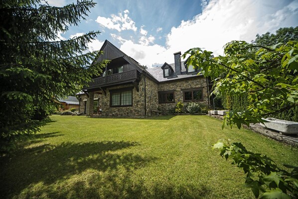 A stone house with a balcony, a well-maintained lawn, and surrounding greenery.