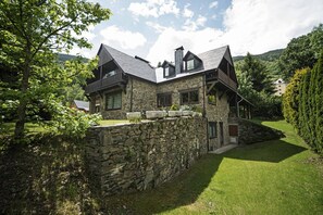 Una casa de piedra con techo inclinado, un balcón y un muro de piedra.