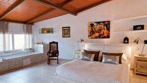 Um quarto espaçoso com uma cama grande, janela com vista, uma cadeira e mesa de cabeceira com abajur.