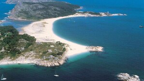 An aerial view of a coastal area with a sandy beach, rocky outcrops, and clear blue waters.