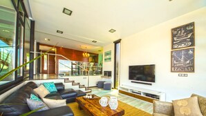 A modern living room with a sofa, coffee table, and TV. There is a staircase leading to an upper level.