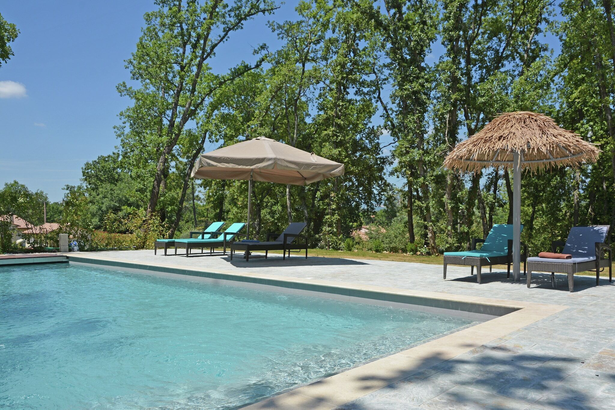 A swimming pool with lounge chairs and umbrellas, surrounded by trees.