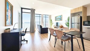 A modern living space with a dining area, kitchen, and a large window offering a city view. - Beautiful Cambodian Inspired Apt with Pool & Gym (Adelaide)