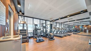 A modern gym with cardio machines, weight stations, and a large mirror. - Beautiful Cambodian Inspired Apt with Pool & Gym (Adelaide)