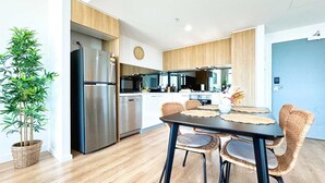 A modern kitchen with a stainless steel refrigerator, wooden cabinets, and a dining area with wicker chairs. - Beautiful Cambodian Inspired Apt with Pool & Gym (Adelaide)