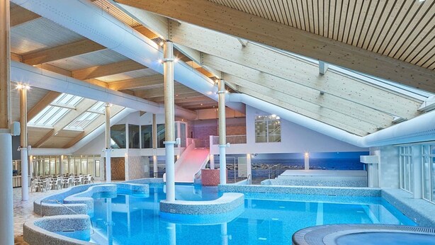 Una piscina interior con tobogán, zonas de descanso y vistas al mar.