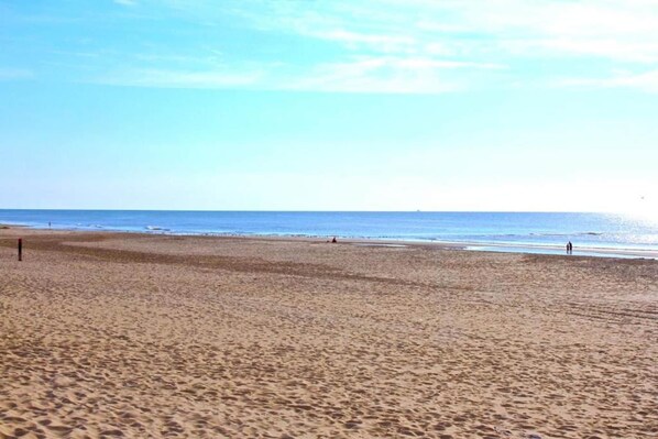 A wide sandy beach with a clear sky and calm sea.