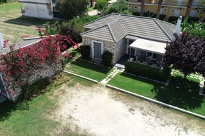 A stone house with a tiled roof, surrounded by a well-maintained lawn and flowering plants. - Villa near Sea in Agrilia (Αgrilia)
