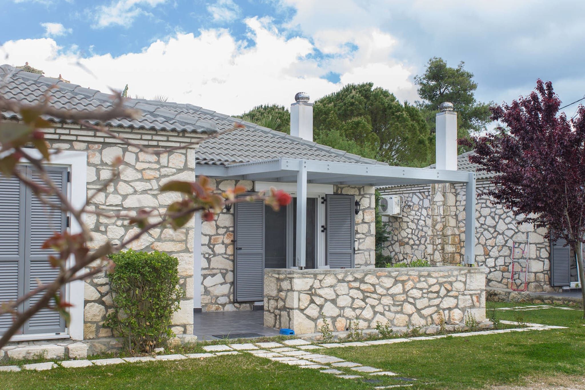 Une maison en pierre avec un toit en tuiles, une véranda et un petit jardin.