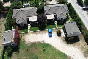 A residential area with two houses, each with a sloped roof and a covered front porch. A blue car is parked in the driveway. - Villa near Sea in Agrilia (Αgrilia)