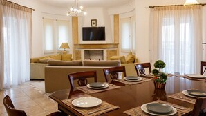 Ein Essbereich mit einem Holztisch, gedeckt für vier Personen, einem Sofa im Hintergrund und einem Fernseher über einem Kamin.