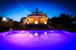 A circular building with a pool in front, illuminated by purple lights.