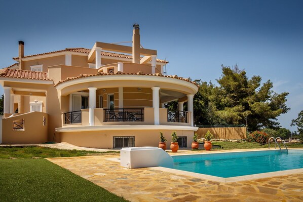 A two-story house with a swimming pool, outdoor furniture, and a well-maintained lawn.