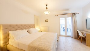 Ein Hotelzimmer mit einem großen Bett, einem Schreibtisch und einem Stuhl. Ein Fenster mit Vorhängen und eine Klimaanlage sind darüber angebracht.