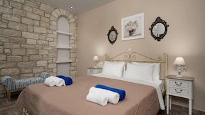 Un lit bien fait, avec des serviettes blanches et bleues, un mur en pierre et un banc en bois.