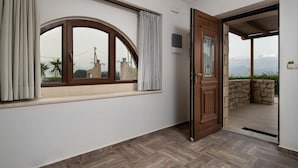 Une pièce dotée d’une grande fenêtre en arc de cercle, d’une porte en bois donnant sur un espace extérieur et d’un mur en pierre.