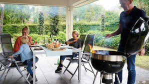 Un área de comedor al aire libre techada con una parrilla, sillas y una mesa lista para una comida.