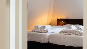 Habitación de hotel con dos camas, cada una con toallas blancas impecables y un cabecero oscuro.