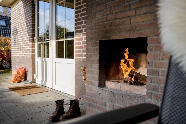 Una chimenea de ladrillo con fuego encendido, un par de botas en el suelo y una puerta blanca con paneles de vidrio.