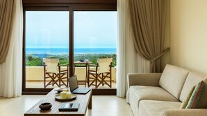 A room with a view of the sea, a sofa, a table with a laptop, and two chairs.