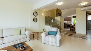 A living room with a sofa, armchair, coffee table, and a staircase leading to a kitchen.