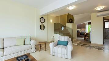 Una sala de estar con sofá, sillón, mesa de centro y una escalera que lleva a una cocina.