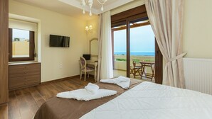 A hotel room with a bed, a desk, a chair, a TV, and a view of the sea.