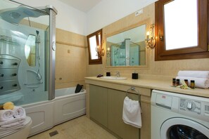 Un baño moderno con ducha envuelta en vidrio, una bañera, un lavabo, un espejo y una lavadora.