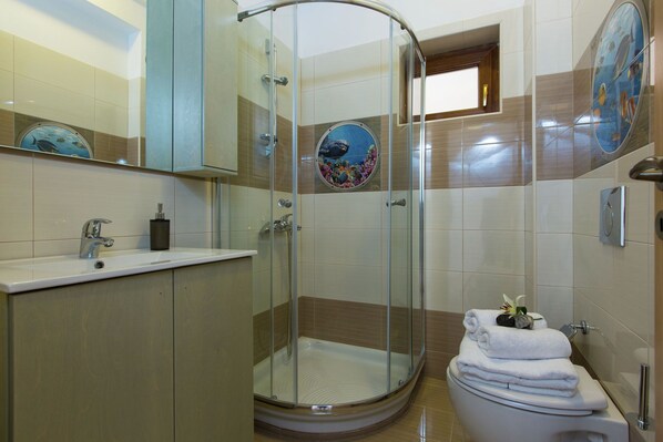 A bathroom with a glass-enclosed shower, a sink, and a toilet.