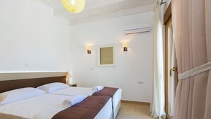 A hotel room with two beds, a window with curtains, an air conditioning unit, and wall-mounted lamps. - Villa in Crete with Private Pool & Beaches Nearby (Achlades)