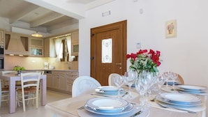 A dining area with a wooden table set for six, surrounded by chairs. A vase with red flowers is on the table. - Villa in Crete with Private Pool & Beaches Nearby (Achlades)