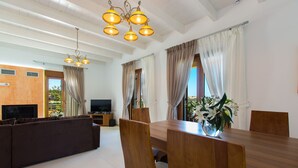 A modern living room with a wooden dining table, a sofa, and a TV. - Villa in Crete with Private Pool & Beaches Nearby (Achlades)