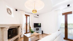 A living room with a fireplace, a television, a sofa, and a ceiling light. - Villas in Crete with Private Pool & Beaches (Achlades)