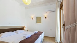 A hotel room with two beds, a window, an air conditioning unit, and a door with curtains. - Villas in Crete with Private Pool & Beaches (Achlades)