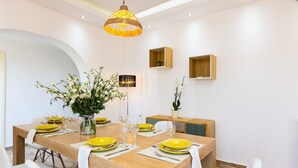 A dining area with a long wooden table set for six, white chairs, yellow plates, and a vase of white flowers. - Villas in Crete with Private Pool & Beaches (Achlades)