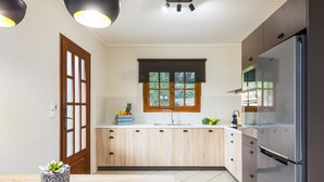 Una cocina moderna con alacenas de madera clara, un refrigerador de acero inoxidable y una ventana con persiana oscura.