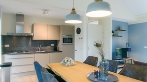A modern kitchen with a wooden dining table, chairs, and pendant lights. - Terraced Home in Netherlands near Veluwe (Voorthuizen)