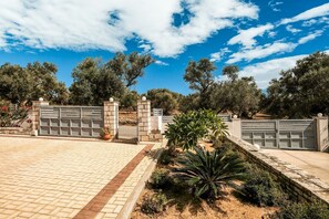 A gated entrance with a paved driveway leading to a building, surrounded by trees and landscaping.